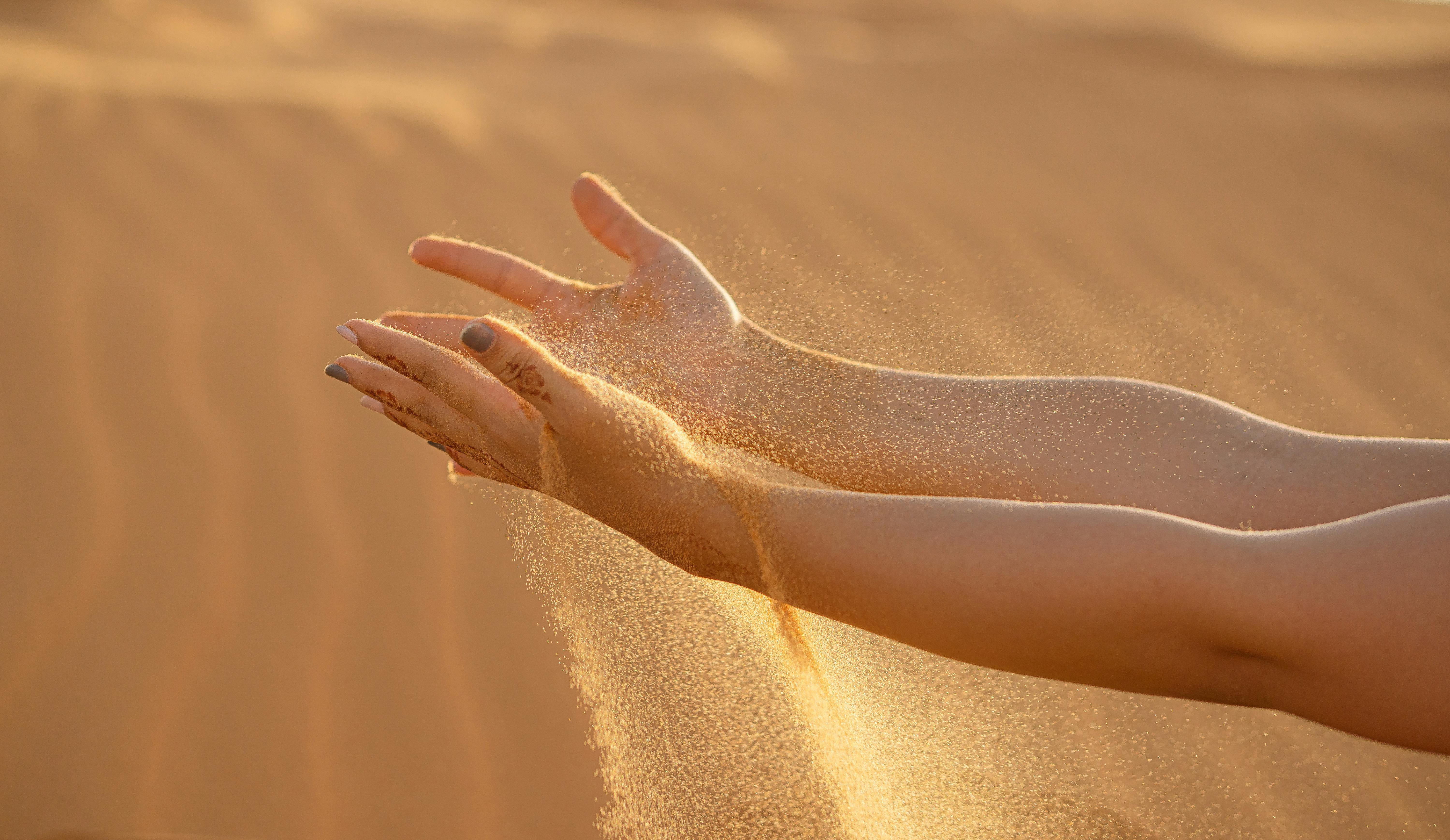 Mains ouvertes laissant couler du sable, symbole du lâcher-prise et du retour à l’essentiel